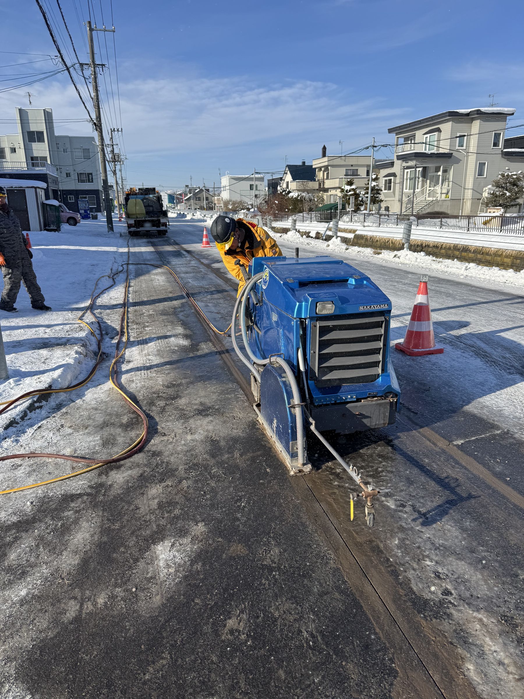 雪の残る道路をカッターで切断する職人